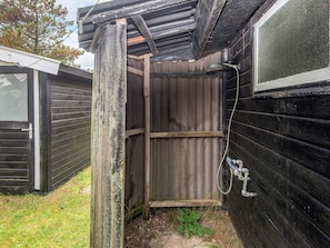 A small wooden structure with a metal door and a window, surrounded by grass and trees.