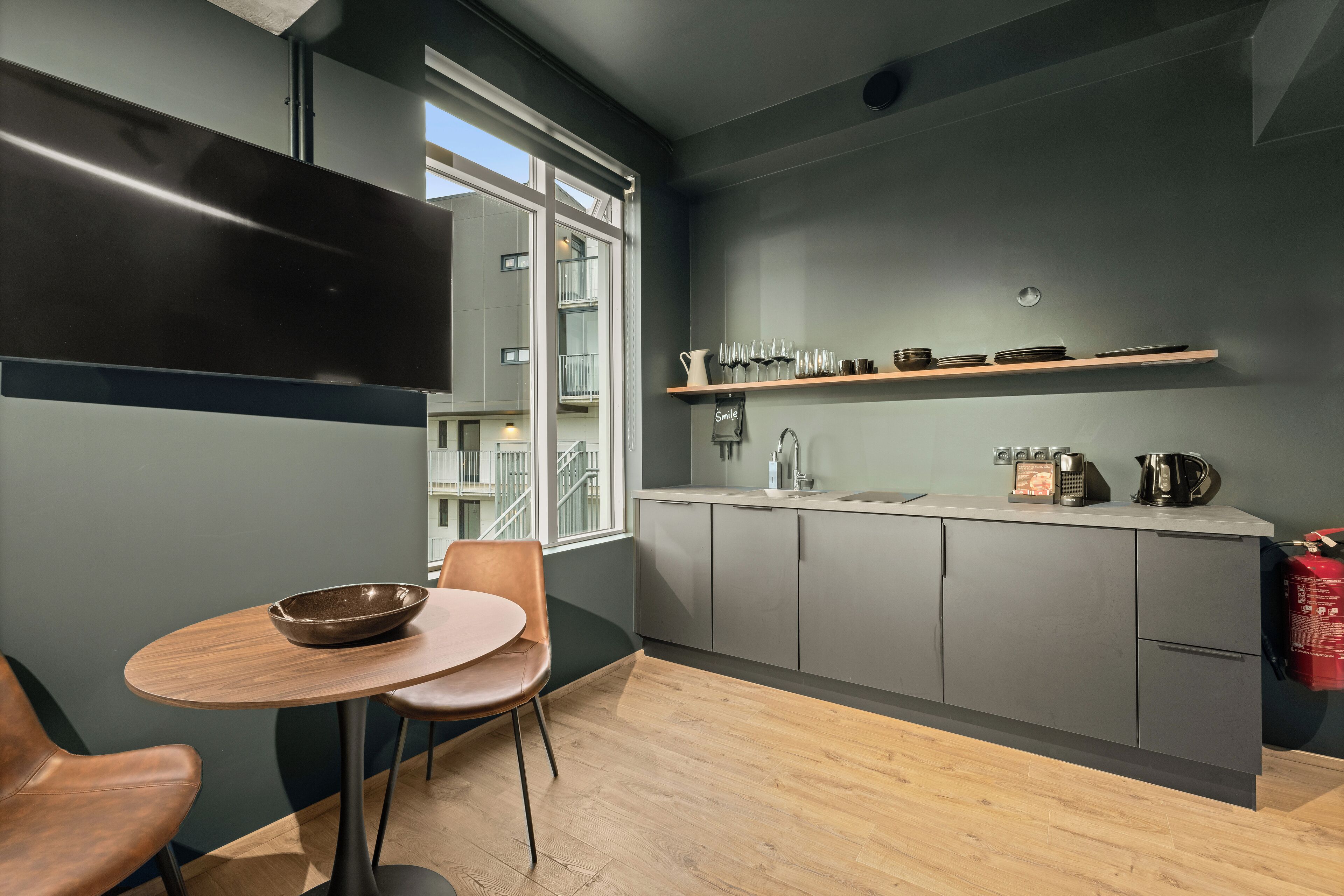 Una cocina moderna con armarios grises, una mesa de comedor de madera y una ventana con vistas a un balcón.