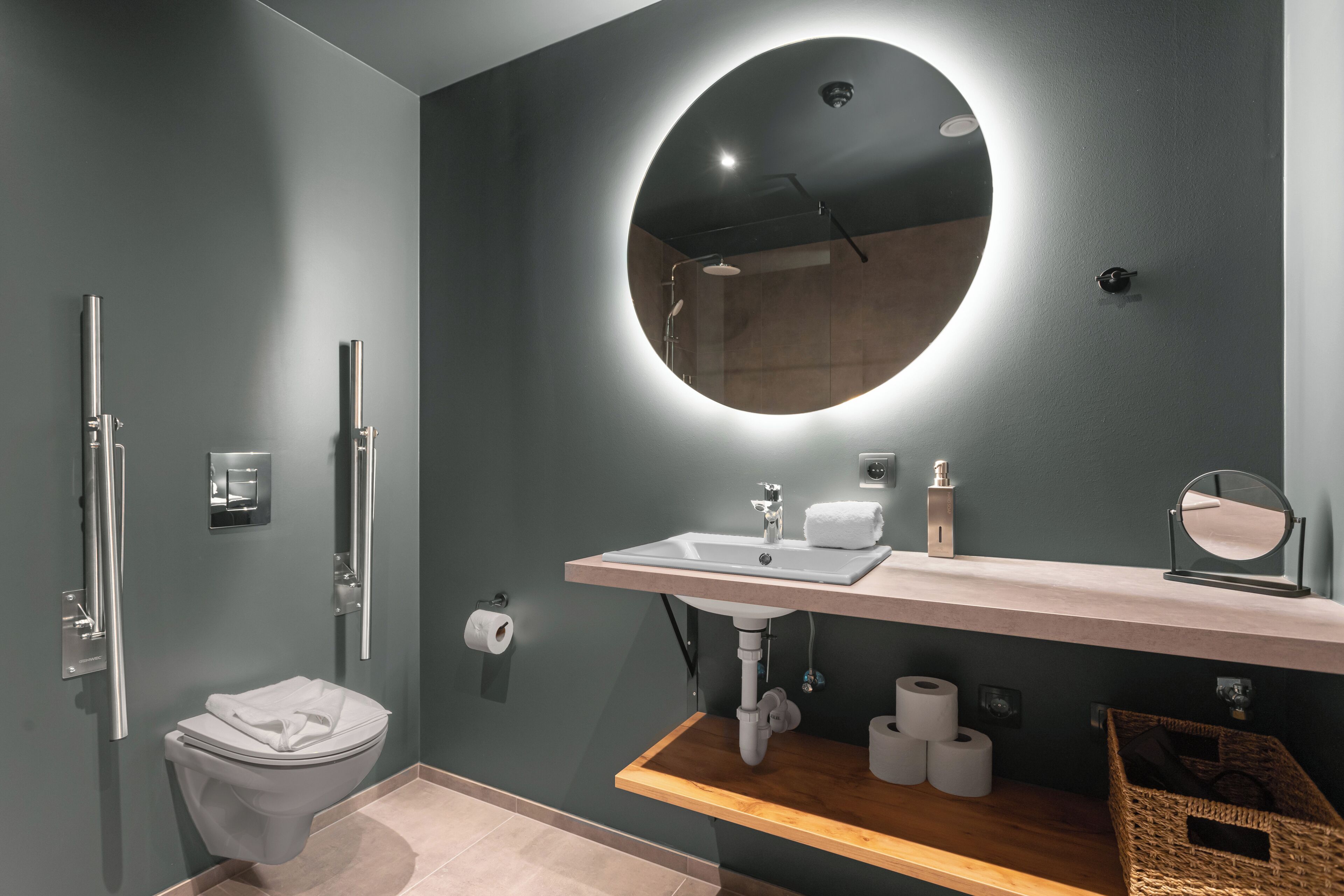 Une salle de bain moderne avec un miroir rond, un lavabo et des toilettes.