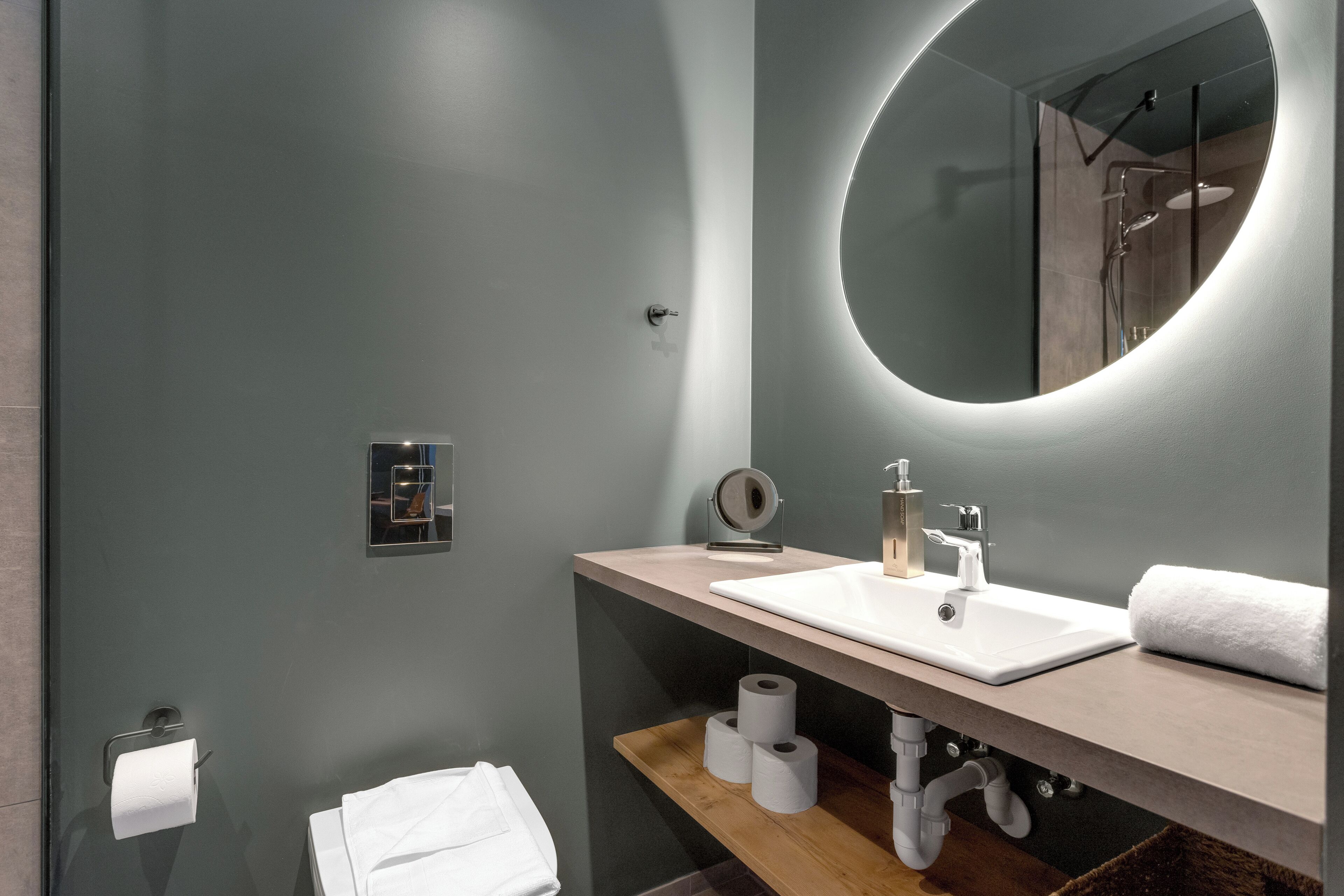 Une salle de bain moderne avec un miroir rond, un lavabo et des toilettes.