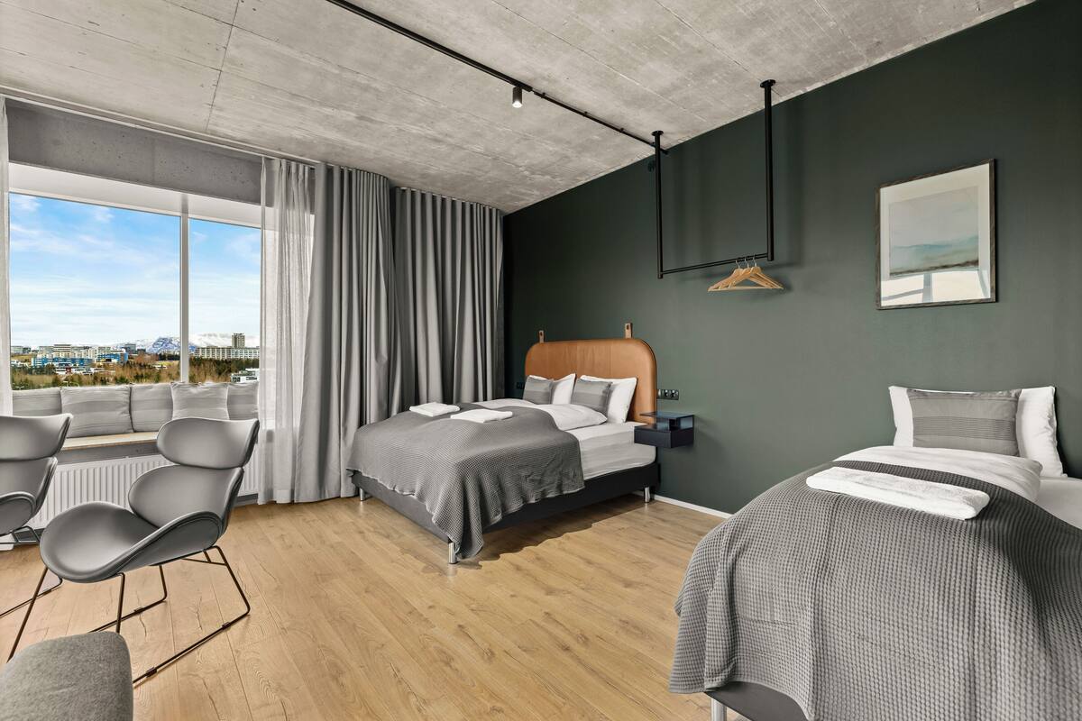 A modern hotel room with a large bed, a smaller bed, a seating area, and a view of the city.