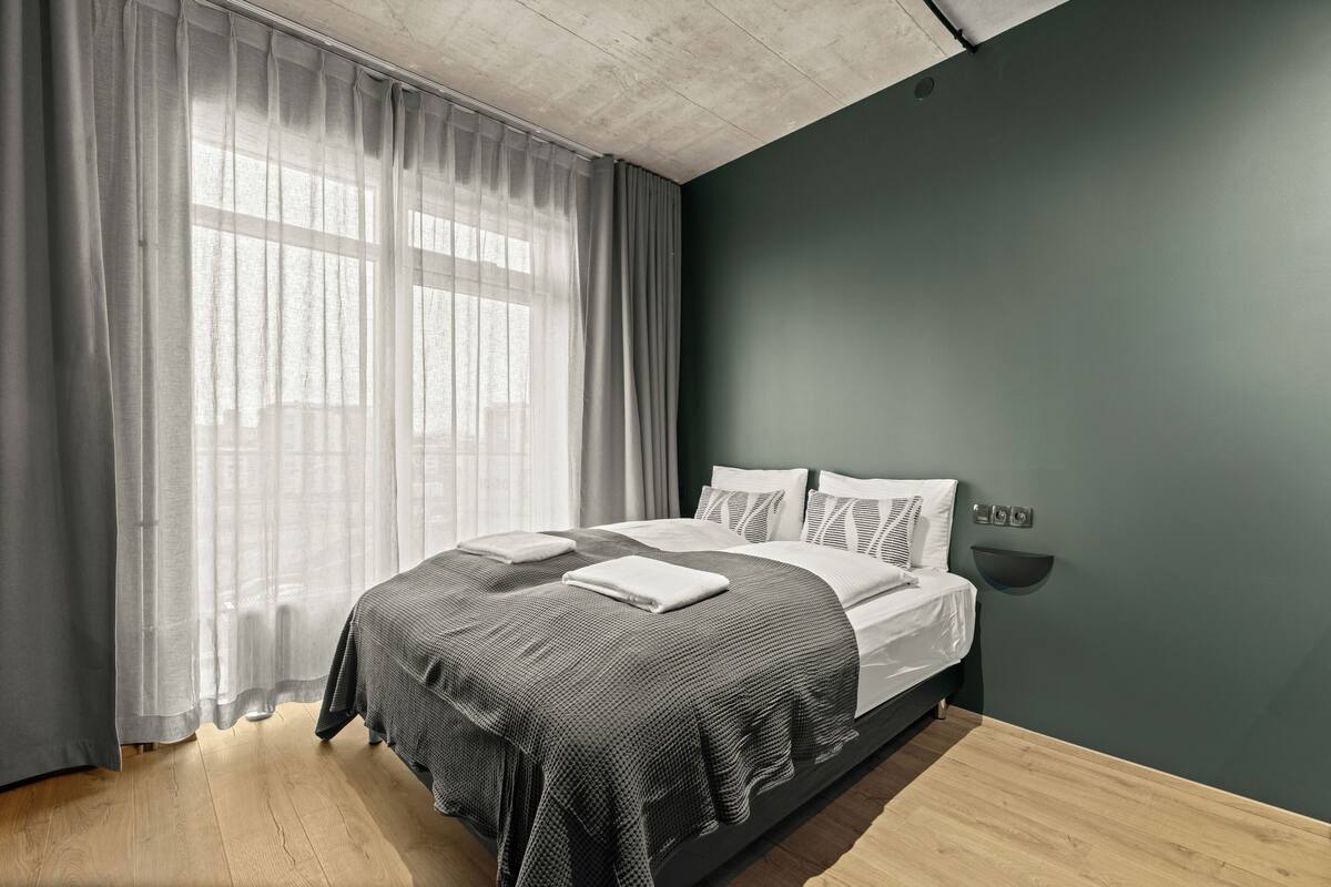A modern bedroom with a bed, curtains, and a wall-mounted light fixture.
