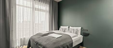 Une chambre à coucher moderne avec un lit, des rideaux et un luminaire fixé au mur.