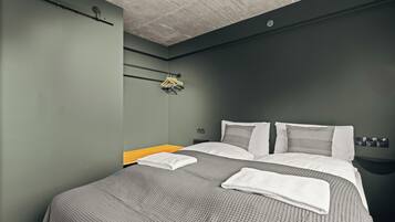 Ein modernes Hotelzimmer mit einem großen Bett, grauer Bettwäsche und einem Nachttisch aus Holz.
