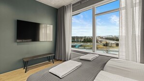 A modern hotel room with a large window, a flat-screen TV mounted on the wall, a bench, and a bed with pillows. - Aurora Nooks (Kópavogur)