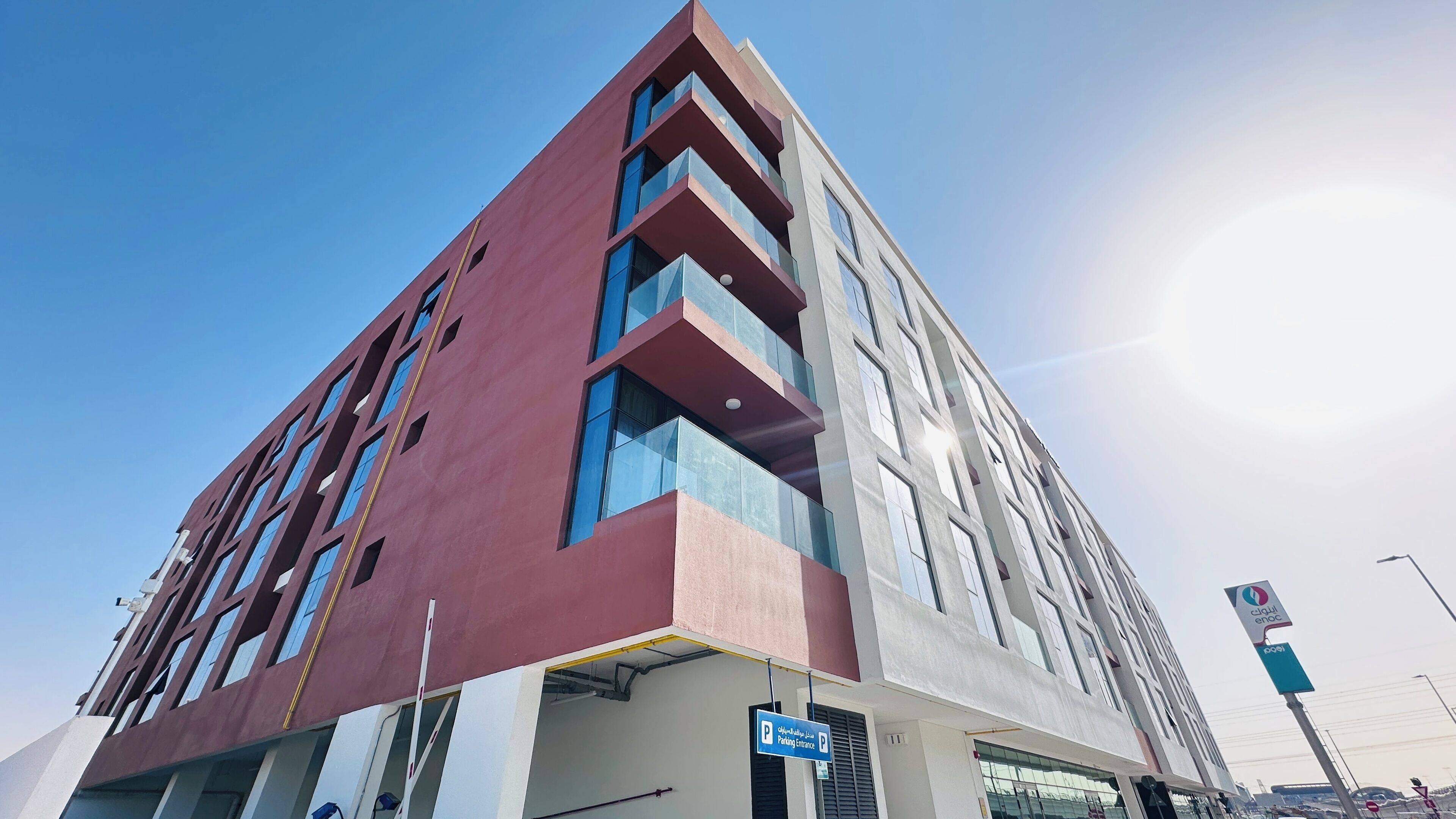Un edificio moderno con una fachada roja llamativa, varios balcones y un cielo despejado.