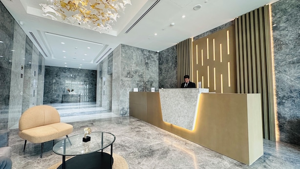 A modern reception area with a marble floor, a reception desk with integrated lighting, a seating area with a glass coffee table, and a decorative ceiling light fixture. - Sunday Sheikh Zayed Road Concord Tower Studio by Belvilla (Dubai)
