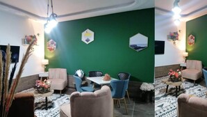 Un espace repas agrémenté d’un mur d’accent vert, d’œuvres d’art murales hexagonales et de différents types de sièges, notamment des chaises et un canapé.