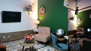 Un salon moderne avec un mur d’accent vert, un téléviseur à écran plat, un canapé beige, un fauteuil bleu et un tapis à motifs.