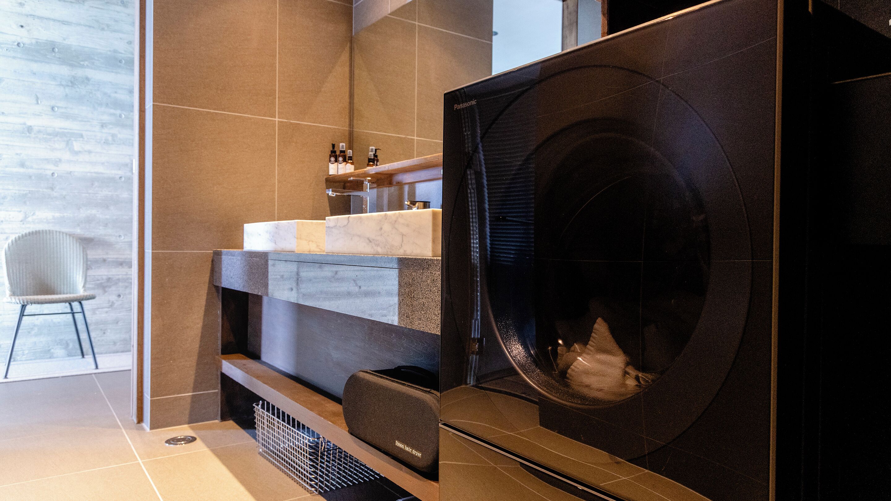A modern bathroom with a large black washing machine, a white chair, and a marble countertop.