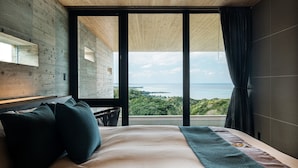 A bedroom with a large window offering a view of the sea and greenery. - ILUVIO RESORT MOTOBU (Motobu)