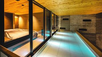 A modern spa room with a glass-enclosed bed, a wooden ceiling, and a stone wall.