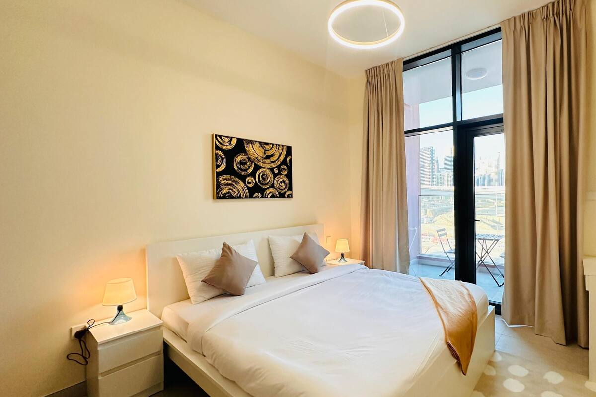 Ein Hotelzimmer mit einem großen Bett, einem Nachttisch mit Lampe, einem Fenster mit Vorhängen und Blick auf die Stadt.