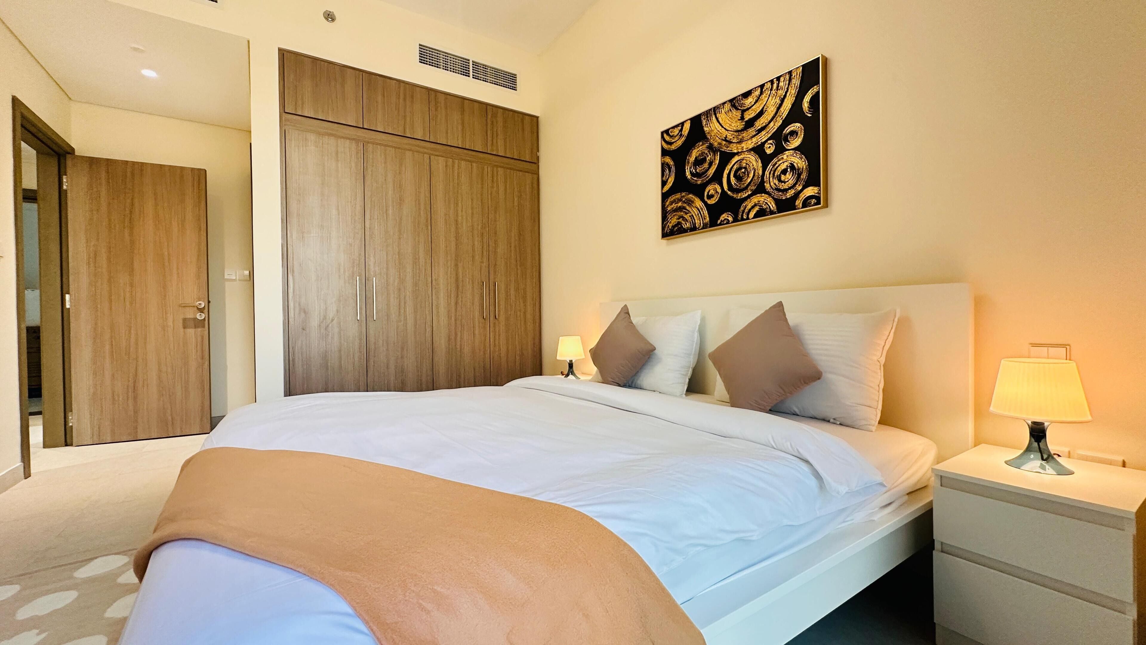 A hotel room with a large bed, a wardrobe, a bedside table with a lamp, and a painting on the wall.