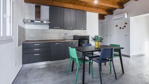 Une cuisine moderne avec des meubles de couleur sombre, un plafond en bois et un coin repas doté de chaises vertes et bleues.