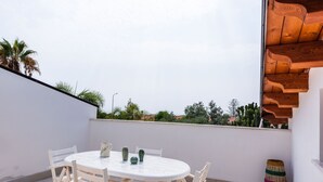 Une table ronde entourée de chaises sur un balcon, un petit cactus et un panier tressé.