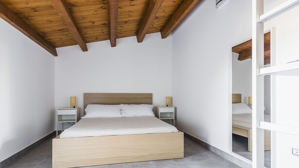 Une chambre à coucher avec un cadre de lit en bois, du linge de lit blanc, deux tables de chevet avec des lampes et un plafond en pente avec des poutres apparentes.