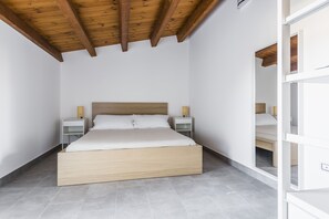 Une chambre à coucher avec un cadre de lit en bois, du linge de lit blanc, deux tables de chevet avec des lampes et un plafond en pente avec des poutres apparentes.