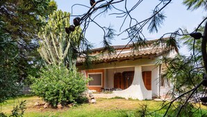 Une maison avec un toit en tuiles, une véranda et un jardin bien entretenu, agrémenté de cactus et de pins.