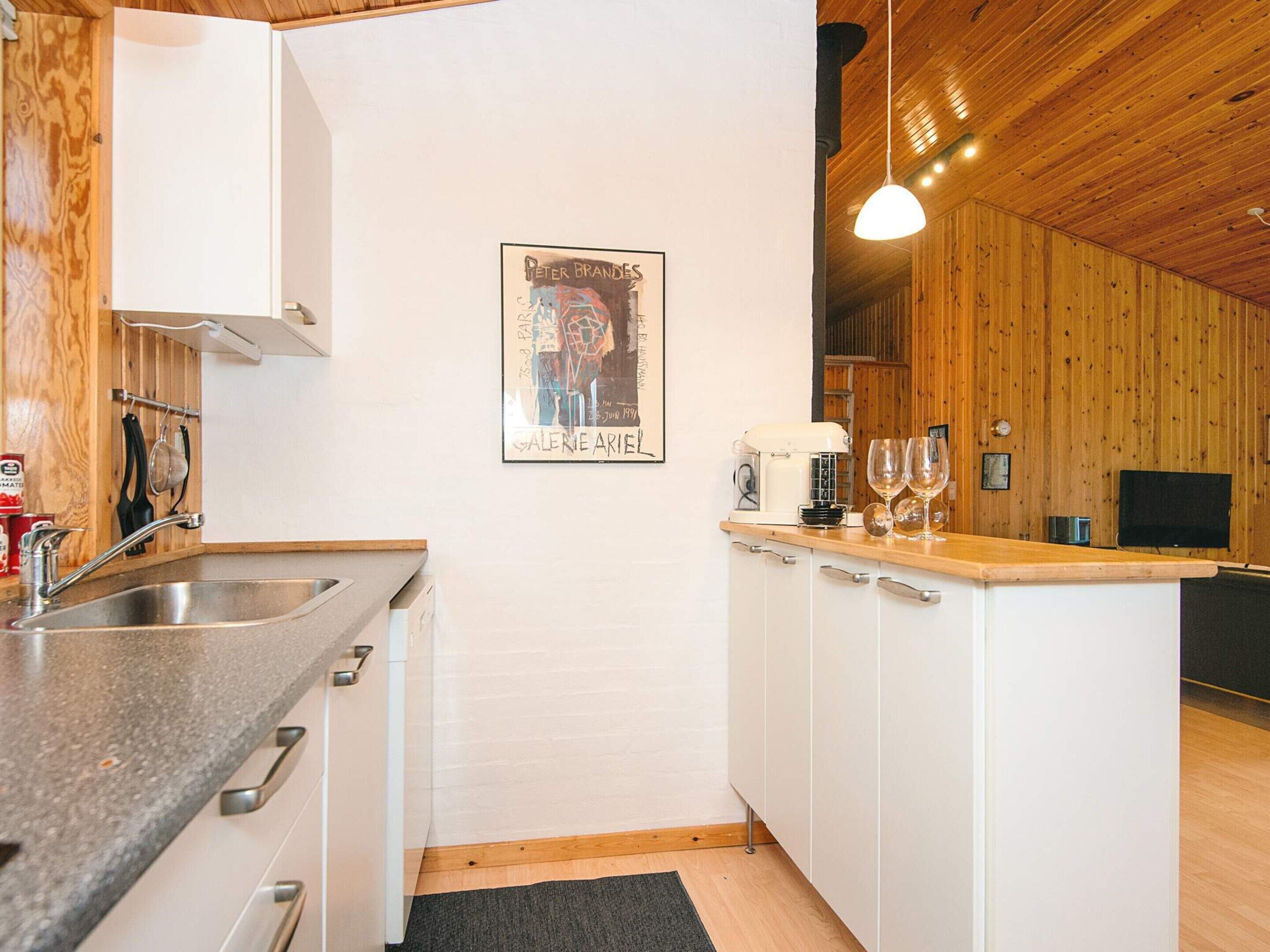Kompakti keittiö, jossa on puinen katto, valkoinen välitila ja pieni keittiösaareke, jossa on kahvinkeitin ja viinilaseja.