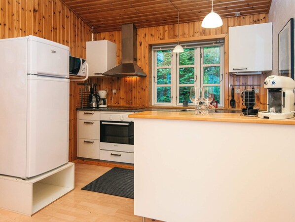 A compact kitchen with wooden walls, a built-in oven, a microwave, and a coffee machine. - 4 Star Holiday Home in Kolind (Kolind)