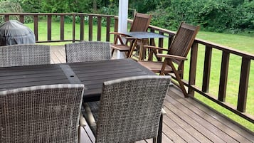 En træterrasse med et bord og stole, omgivet af gelænder og grønne planter.