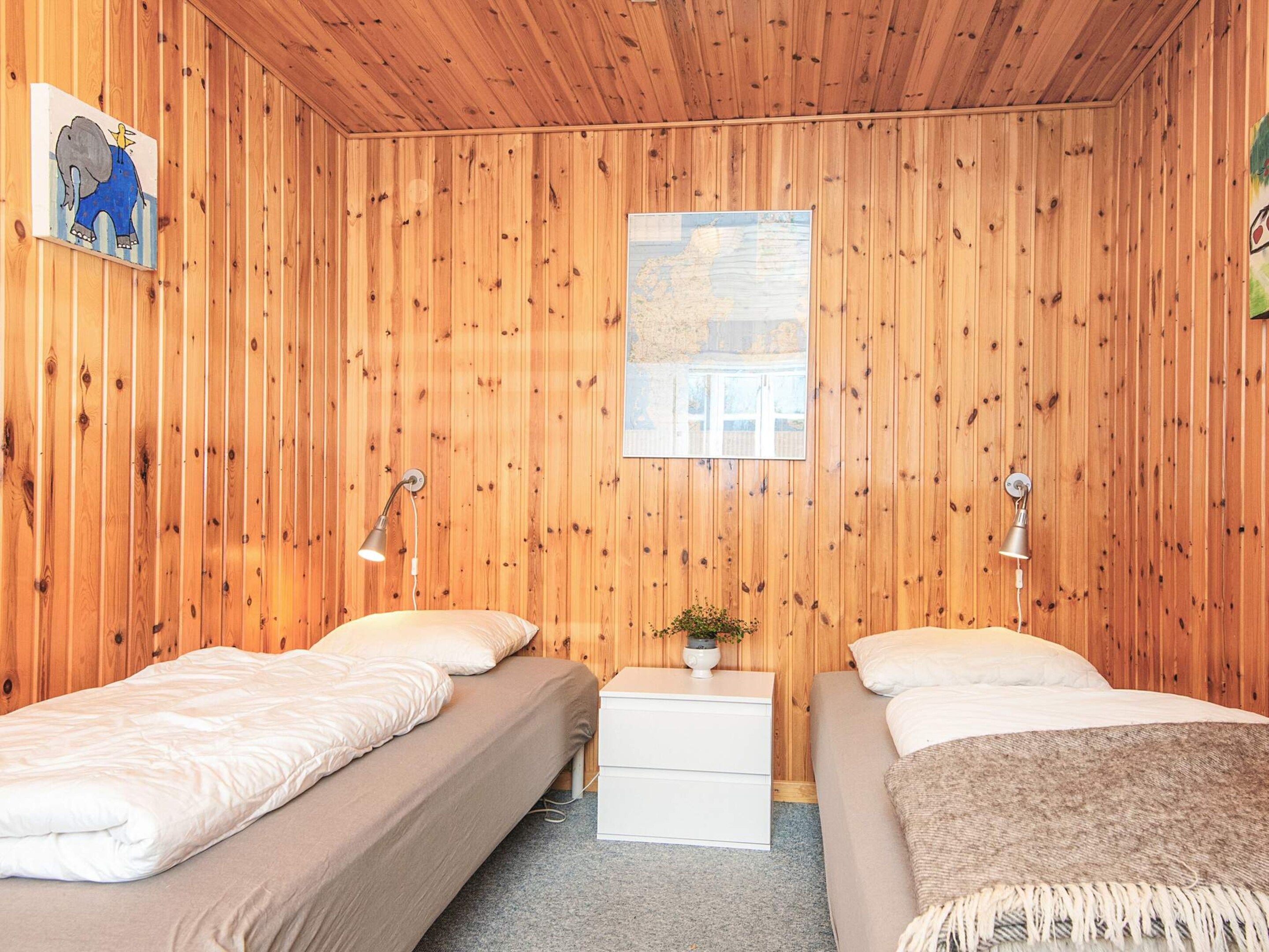 Une chambre aux murs recouverts de lambris en bois, avec deux lits, des lampes de chevet, une petite table sur laquelle est posée une plante, et une carte accrochée au mur.