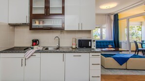 A modern kitchen with white cabinets, a microwave, and a sink. There is a dining area with a blue sofa and a table. - Awesome apartment in Privlaka with house sea view (Privlaka)