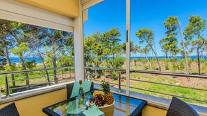 A balcony with a glass table, wicker chairs, and a view of the sea and trees. - Awesome apartment in Privlaka with house sea view (Privlaka)