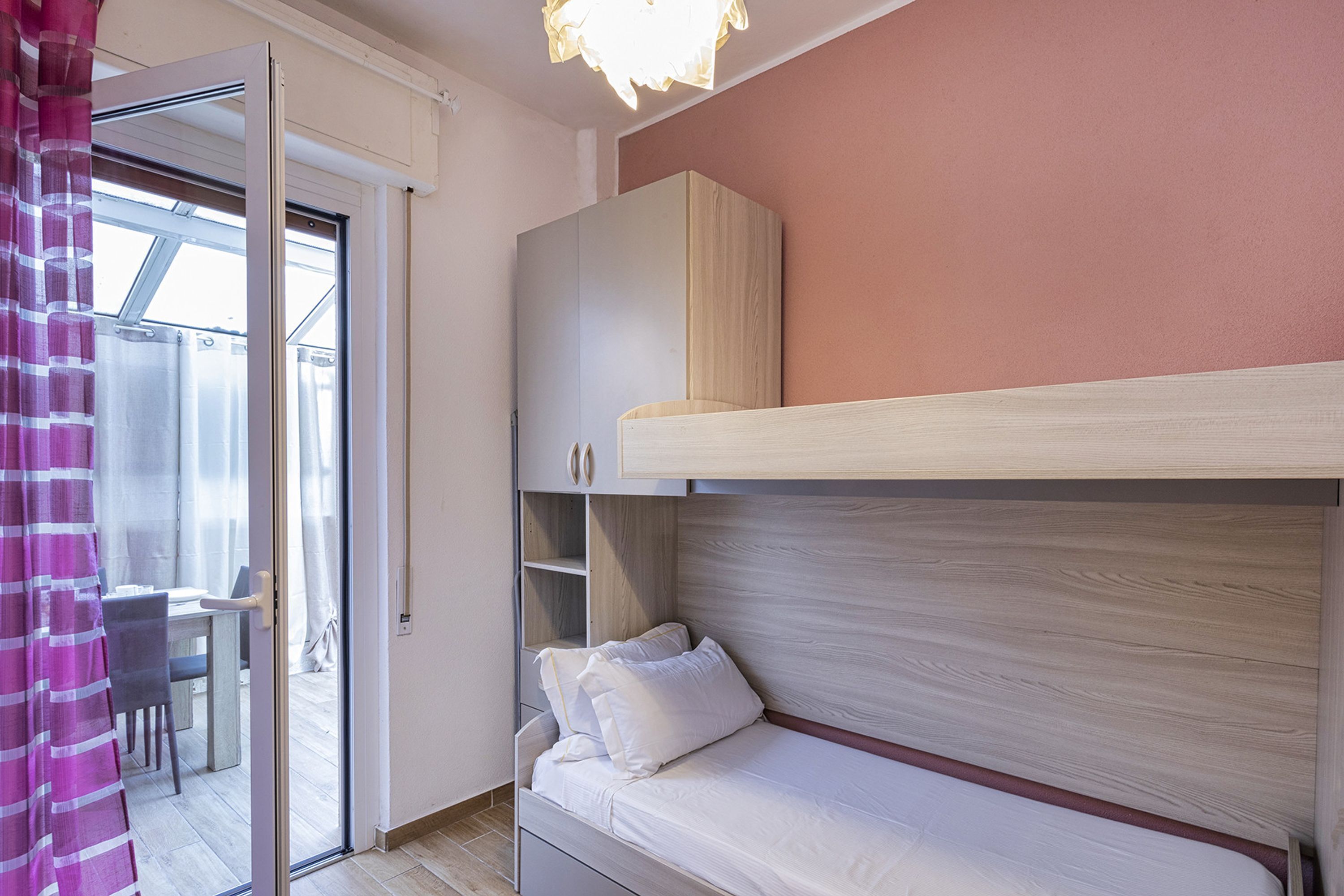A bedroom with a bunk bed, a desk, and a chair in the adjacent room.