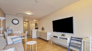 Un salon moderne avec un canapé, des fauteuils, une petite table, un téléviseur et, au fond, un coin cuisine.