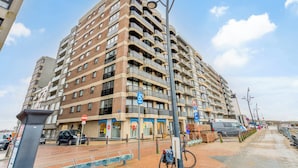 Un immeuble résidentiel à plusieurs étages, doté de balcons, d’un panneau indiquant un espace de stationnement et d’un vélo.