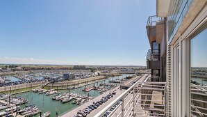 Una marina con numerose imbarcazioni ormeggiate, cielo sereno e un edificio moderno con un balcone.