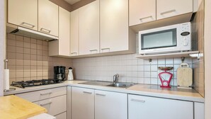 Una cucina moderna con mobili bianchi, un lavello in acciaio inossidabile, un forno a microonde e un piano cottura a gas.