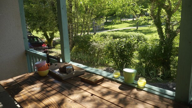 A wooden deck with a table set for breakfast, overlooking a well-maintained garden and a picnic area.