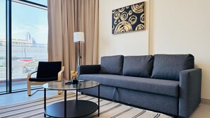A modern hotel room with a grey sofa, a glass coffee table, a black chair, a floor lamp, and a large window with a view of a bridge and buildings. - Sunday Sheikh Zayed Road Concord Tower 2 BR by Belvilla (Dubai)