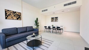 A modern living room with a grey sofa, a glass coffee table, and a dining area with a white table and black chairs.