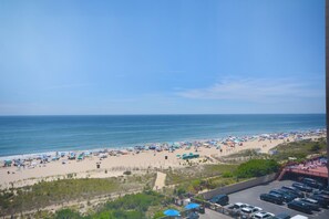 A beach with umbrellas and people, a parking area, and a view of the ocean.