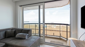 A modern living room with a grey sofa, a large sliding glass door leading to a balcony with a view of the beach. - Apartment in Blankenberge by the Sea (Blankenberge)