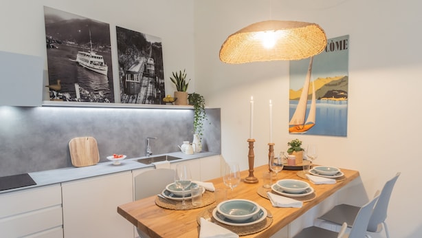 A modern kitchen with a wooden dining table set for four, white chairs, and a hanging wicker lamp. - The Printers Home 2 in Como (Como)