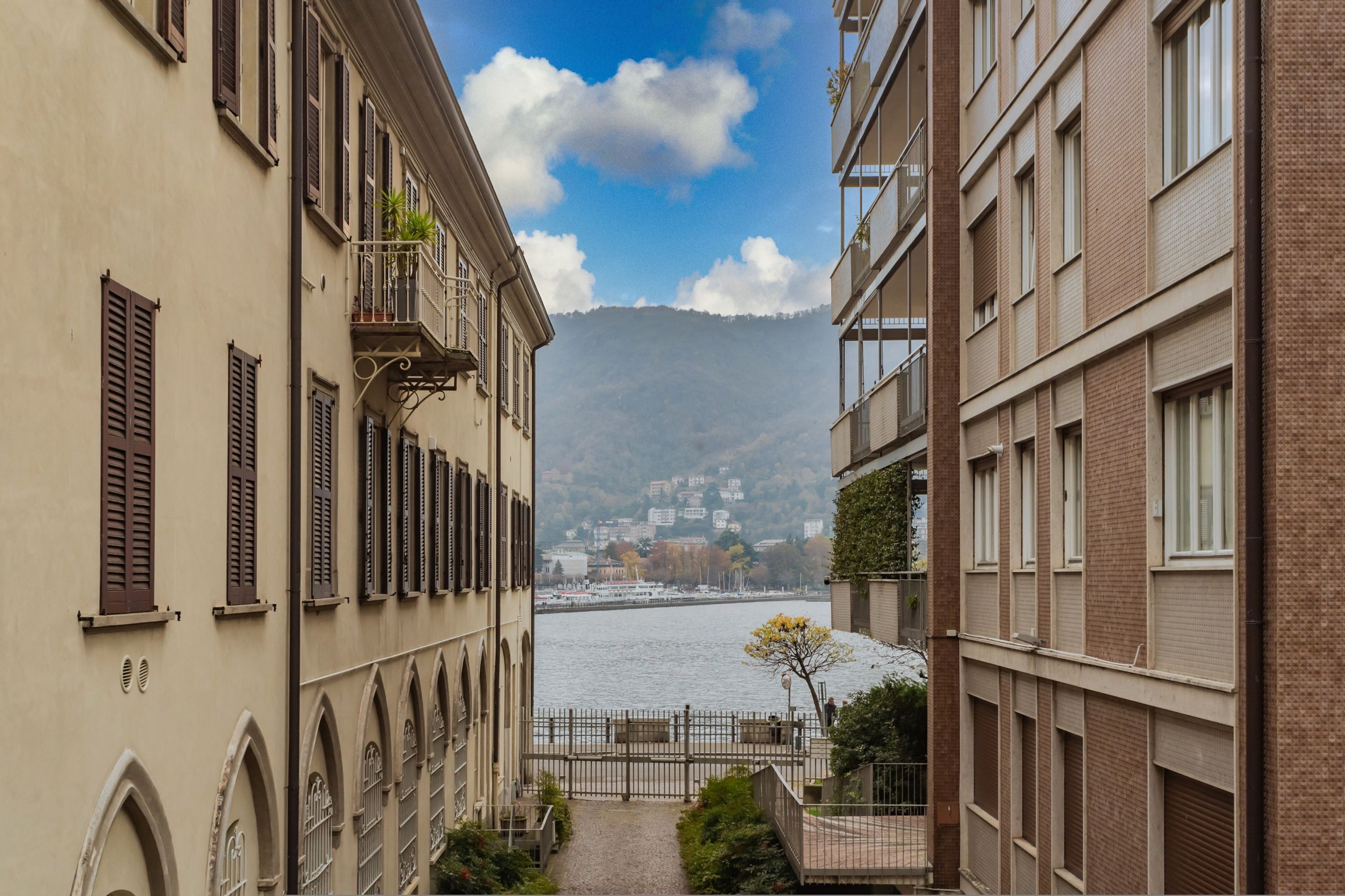 A narrow alleyway between buildings with a river and mountains in the background.