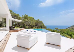 A modern outdoor pool area with white lounge chairs and a wooden deck. - Stylish Villa With Infinity Pool (Sant Josep de sa Talaia)