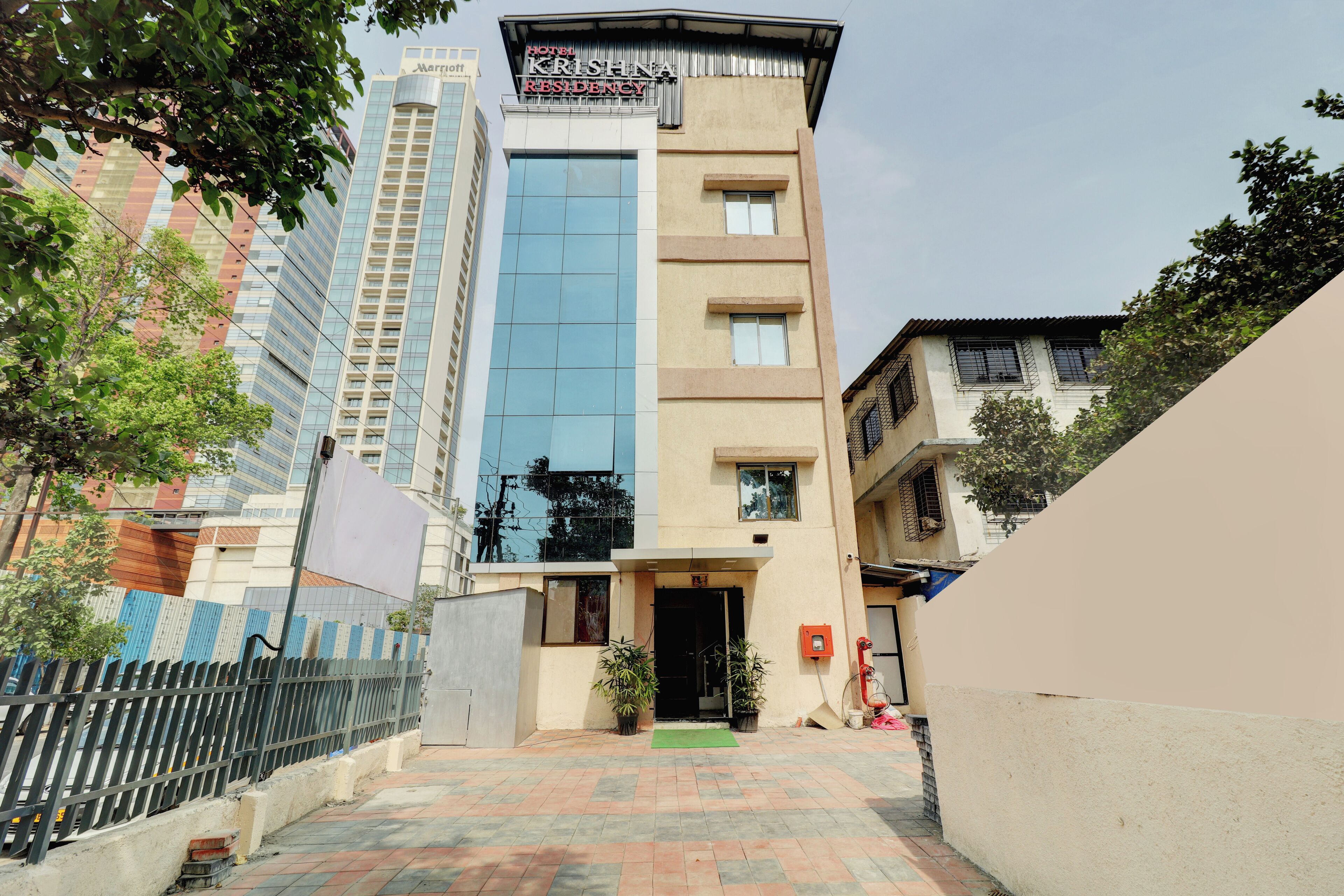 Un hotel llamado 'Hotel Krishna Residency' con una fachada moderna, un acceso con puerta de rejas y un pequeño felpudo verde en la entrada.