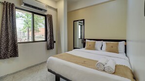 A hotel room with a bed, curtains, an air conditioner, a mirror, and a window with a view of buildings and trees. - Hotel Krishna Residency  (Navi Mumbai)