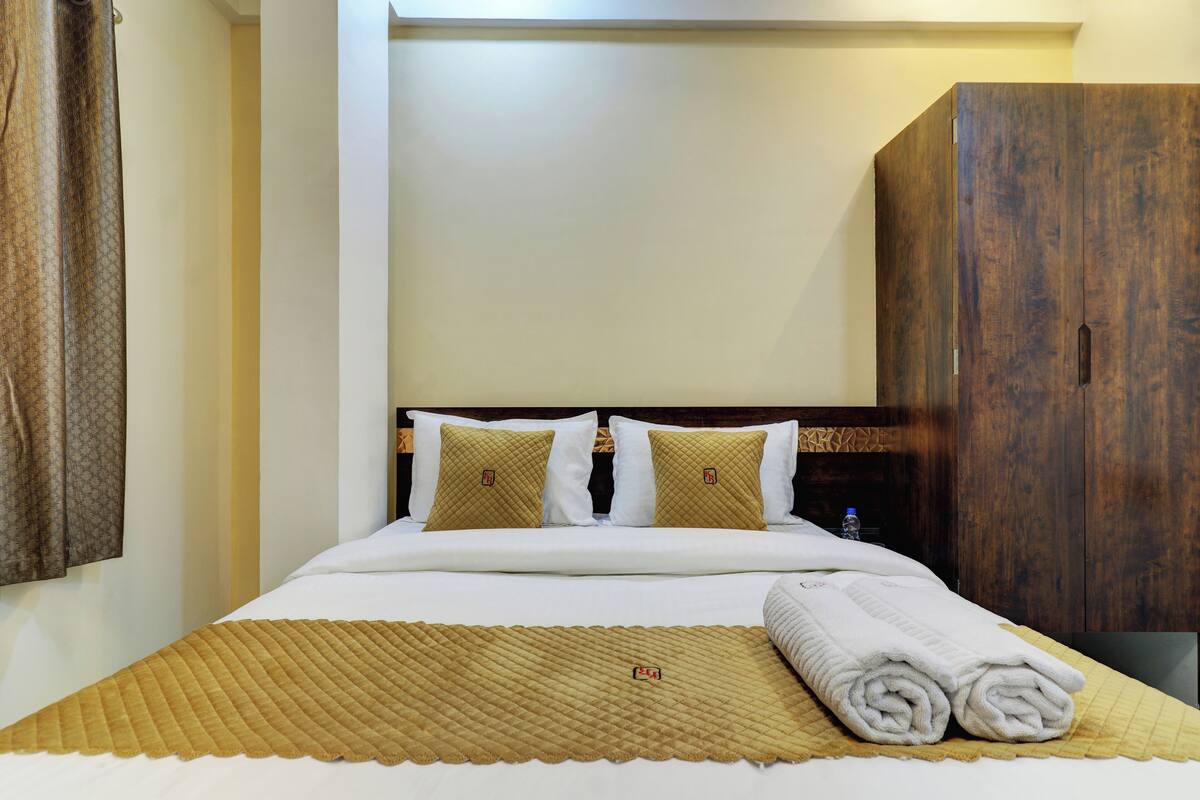 A neatly made bed with a quilted blanket, two pillows, and a rolled towel.