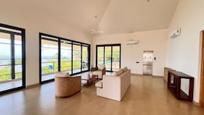 Un salon spacieux doté de grandes fenêtres, d’un canapé, d’une table basse et d’un fauteuil en osier.