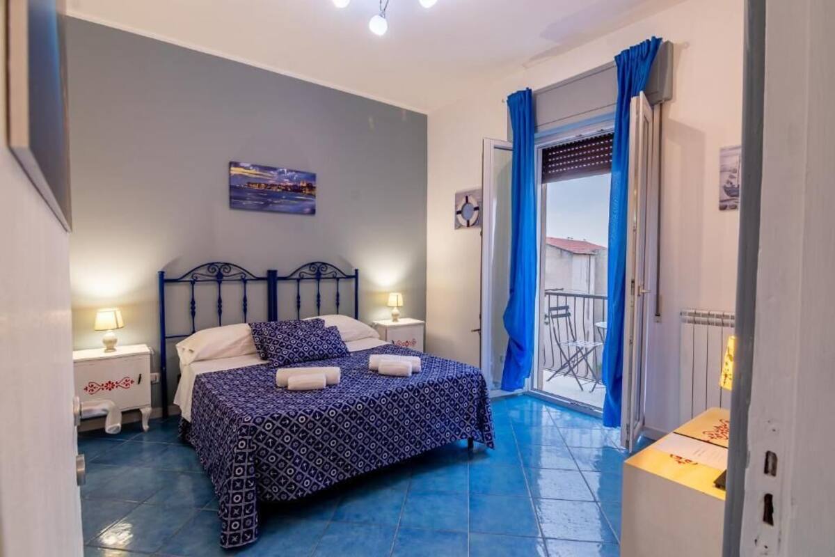 Une chambre à coucher comprenant un lit, deux tables de chevet, une commode, une fenêtre avec des rideaux et une vue sur le balcon extérieur.