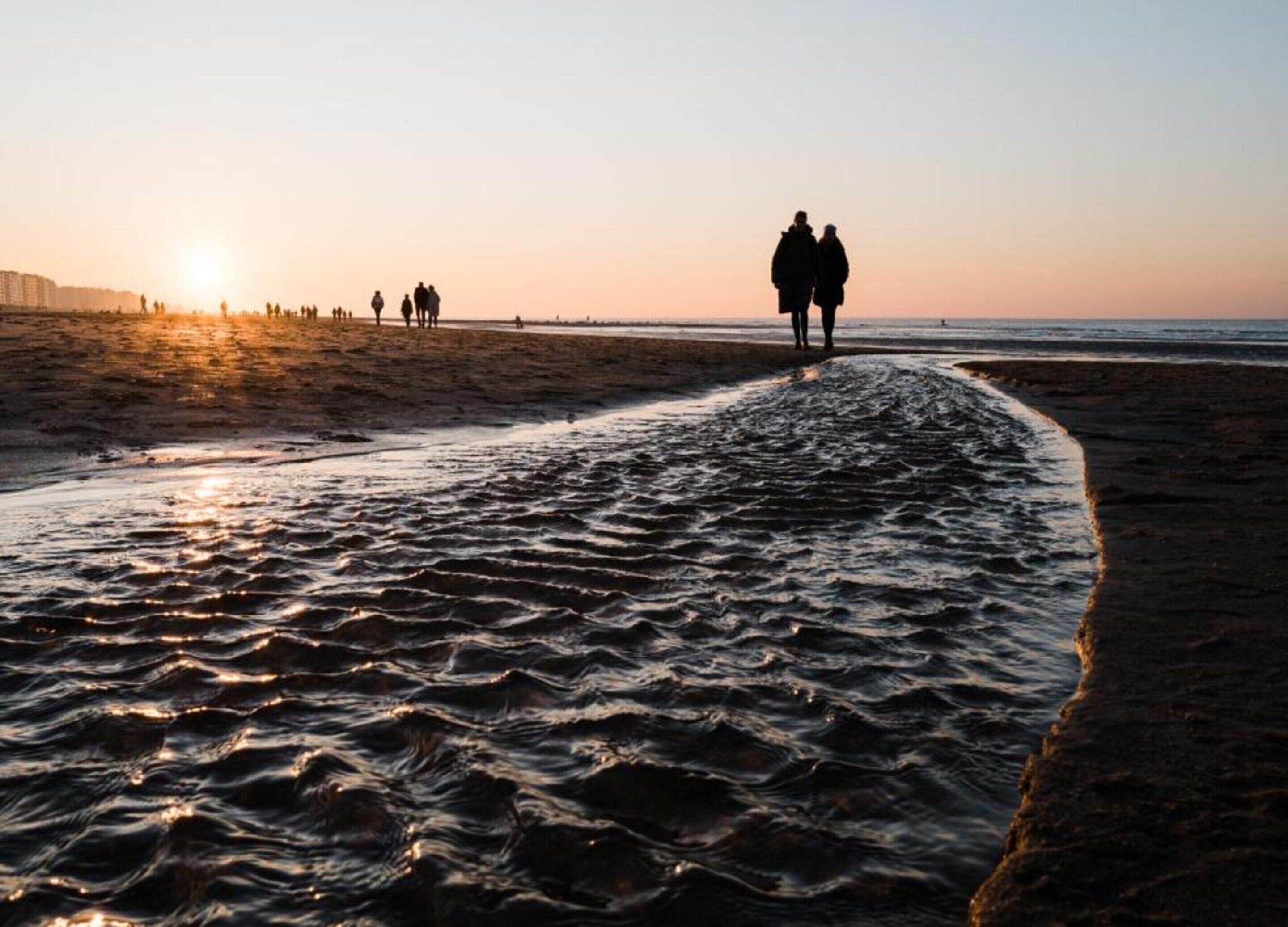 Une plage où des gens se promènent le long du rivage au coucher du soleil.