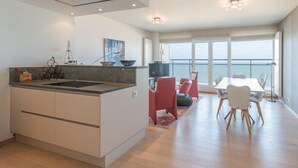 Una cucina moderna con isola centrale, zona pranzo con tavolo e sedie, e un'ampia finestra vista mare.