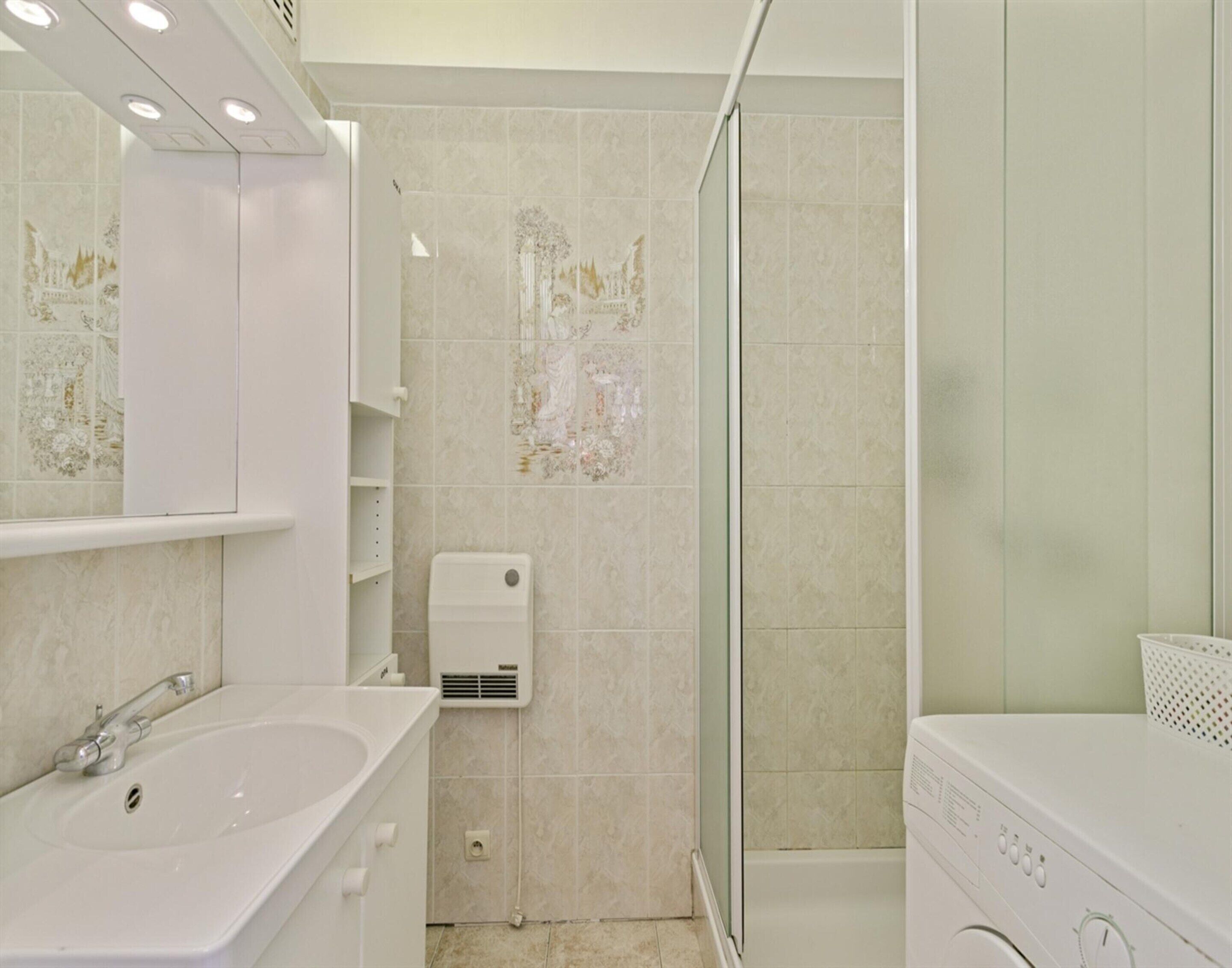 Un baño con lavamanos, espejo, ducha y lavadora blanca.